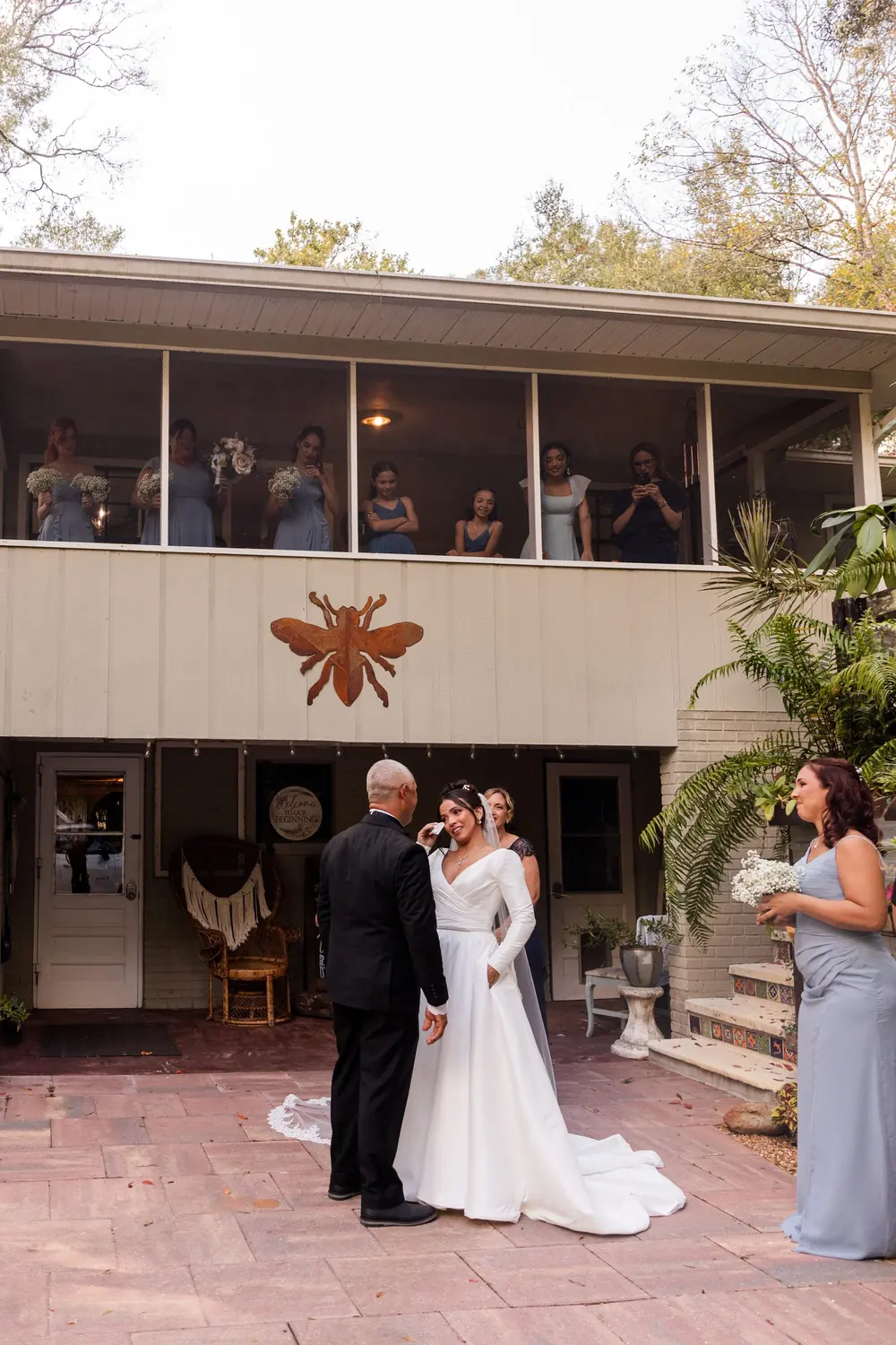First look on the porch, the whole wedding party watching, a bridesmaid photographing from the balcony